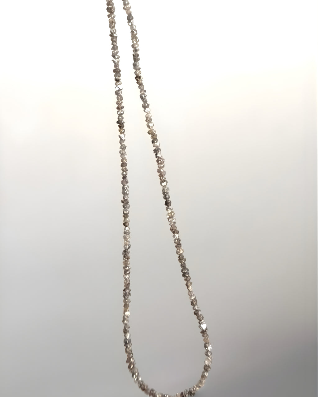 Goldstone & Pebble 3mm natural rough diamond beaded necklace suspended in front of a blank wall. April birthstone. 