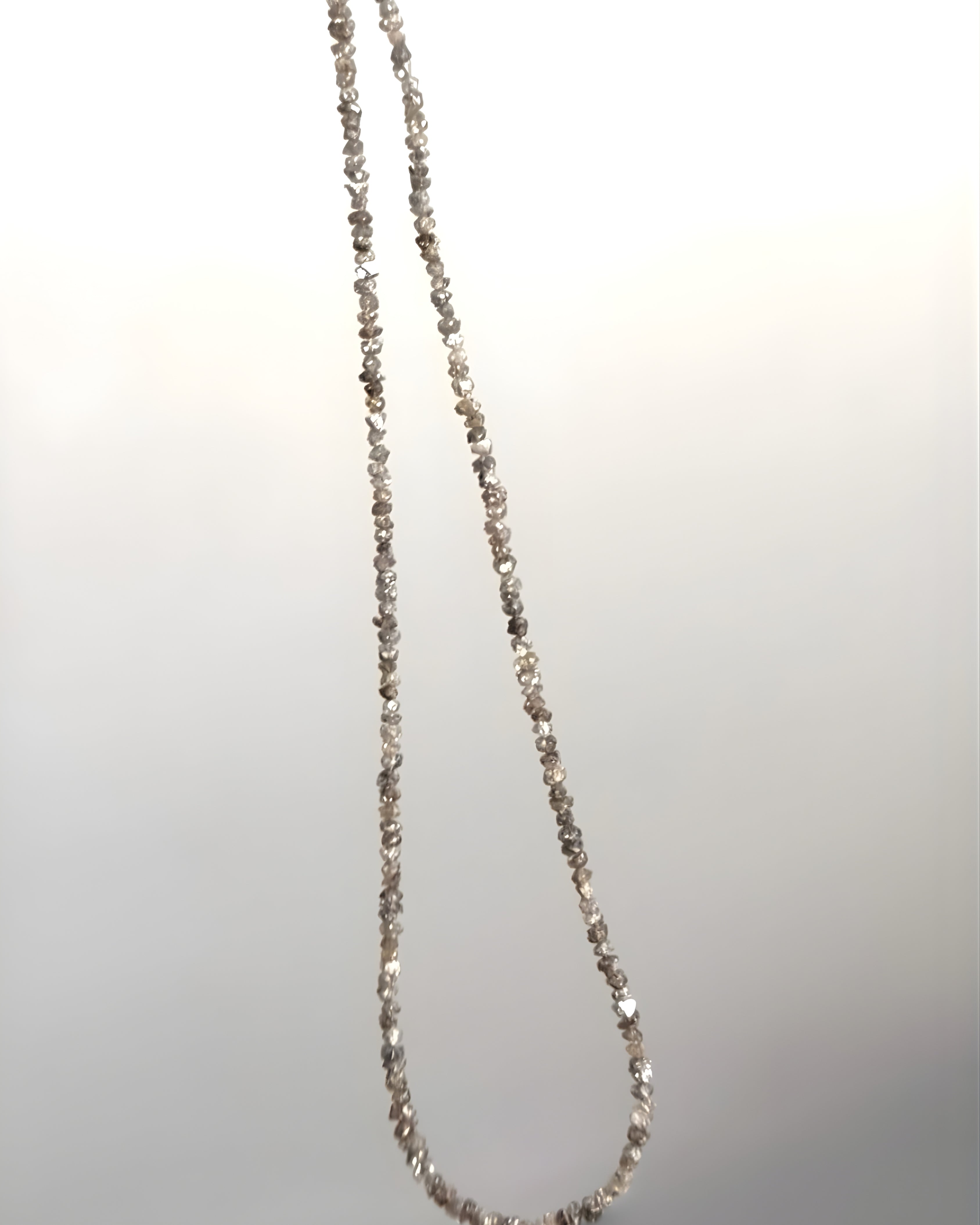Goldstone & Pebble 3mm natural rough diamond beaded necklace suspended in front of a blank wall. April birthstone. 