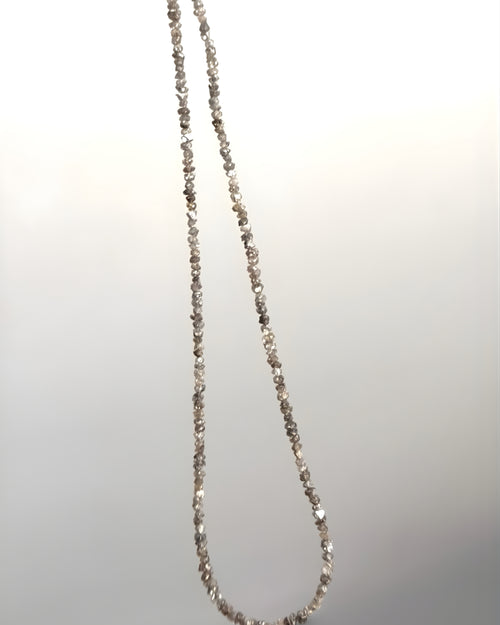 Goldstone & Pebble 3mm natural rough diamond beaded necklace suspended in front of a blank wall. April birthstone. 