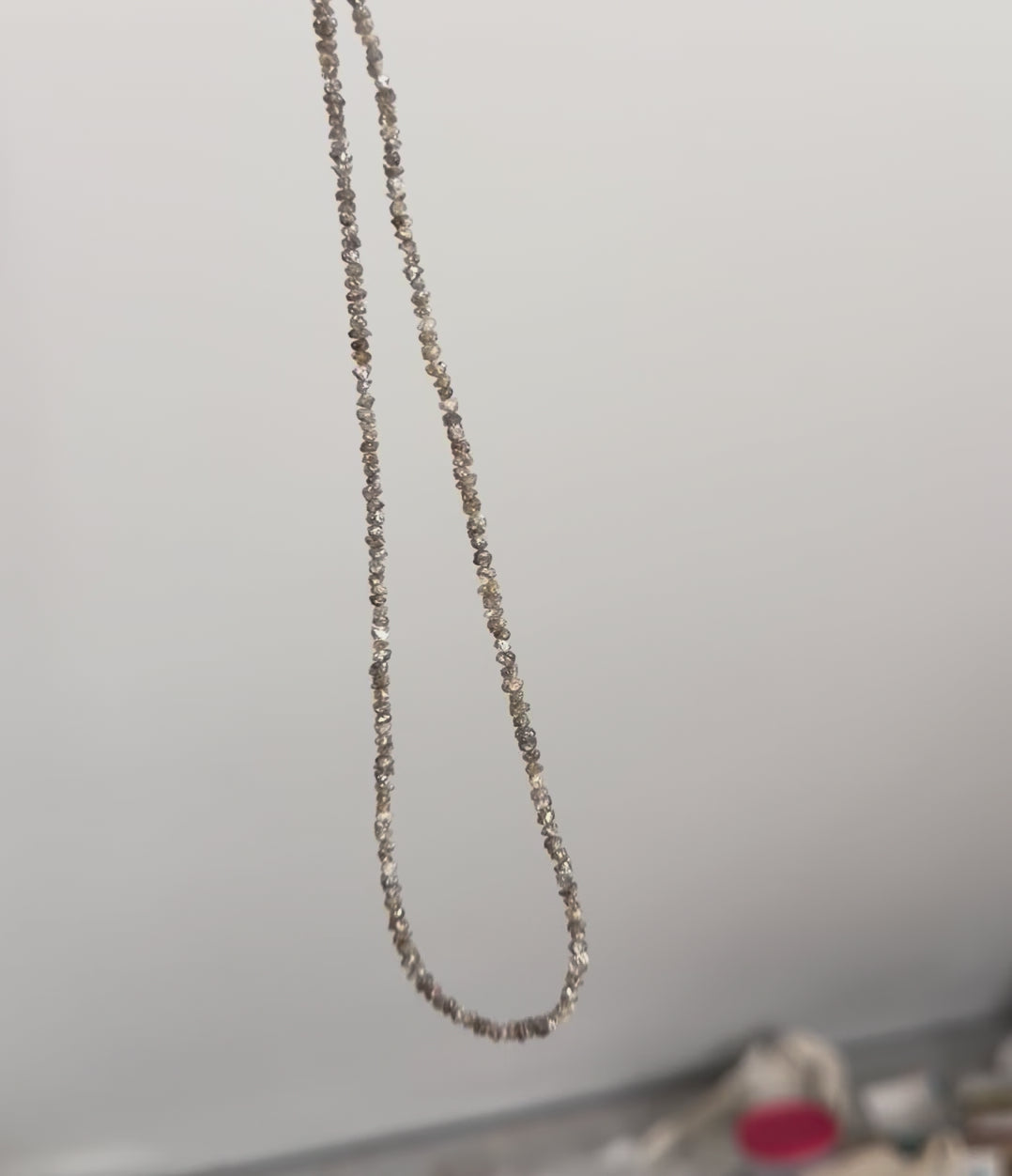 Goldstone & Pebble natural rough diamond necklace hanging infront of blank wall, reflecting light and casting a shimmery sparkle, while evoking a rebelious yet organic feel. 